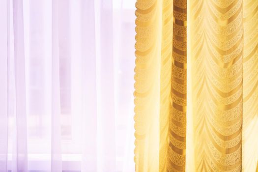 a piece of material suspended at the top to form a covering or screen, typically one of a pair at a window. Golden curtains and tulle on the window in the warm midday sun