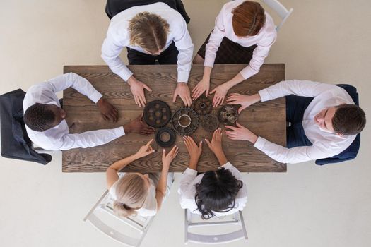 Group of business people joining together metal gears on table at workplace top view