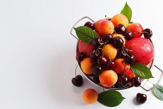 apricots and cherries in a metal bowl on a white background. Copy spase