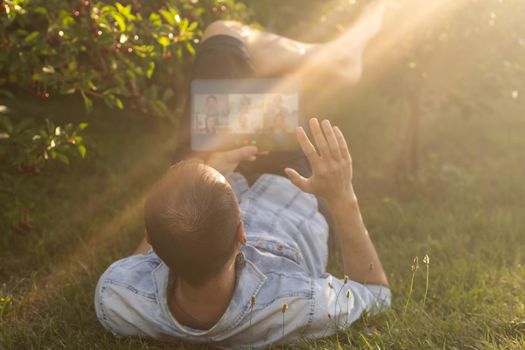 Young man in the garden in summer on the laptop computer while chatting online as a freelancer