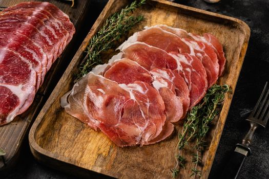 Aged meat jamon, dry cured sausage slices set, on black dark stone table background