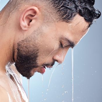 Young mixed race man standing in the shower with water running down his body during his morning grooming routine. Serious hispanic guy rinsing his body with a warm shower practicing good hygiene.