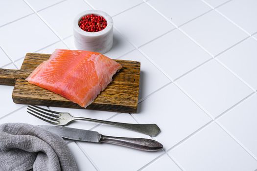 Fresh salmon fillet cut, on white ceramic squared tile table background, with copy space for text