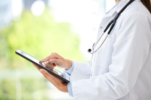 Closeup of female doctor working on her digital tablet in the office. A unknown mixed race and professional young woman working in a hospital office. Health resources are easy to find online.