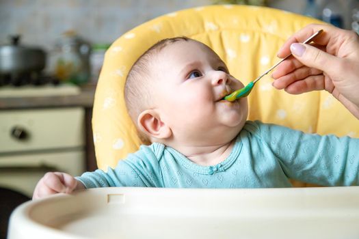 Little baby is eating broccoli vegetable puree. Selective focus. people.