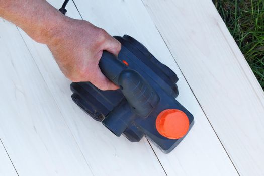 Man sanding wood with orbital sander in workshop