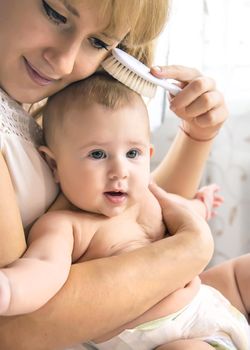 The mother is combing the little baby's hair. Selective focus. People.