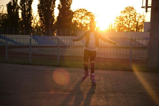 Little pretty happy funny girl on roller skates at stadium at sunset, learning to roller skate outdoors. Outdoor activity for children. Active sport for preschool kid. sun glare, selective focus