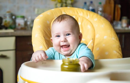 Little baby is eating broccoli vegetable puree. Selective focus. people.