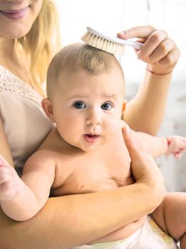 The mother is combing the little baby's hair. Selective focus. People.