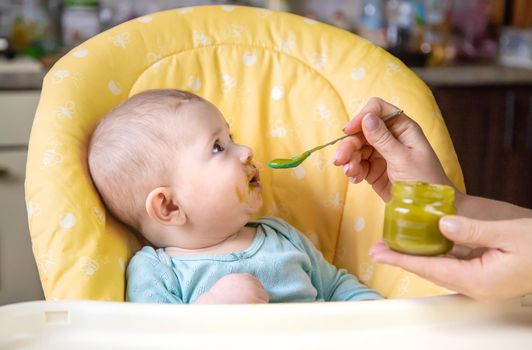 Little baby is eating broccoli vegetable puree. Selective focus. people.