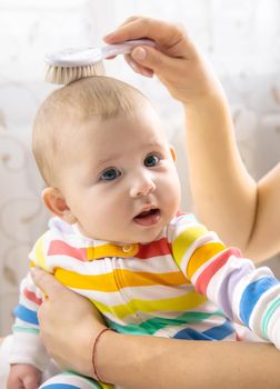 The mother is combing the little baby's hair. Selective focus. People.