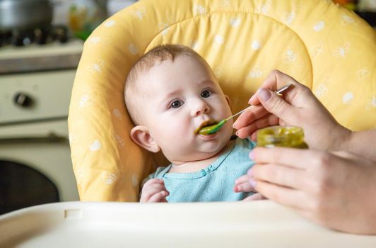 Little baby is eating broccoli vegetable puree. Selective focus. people.