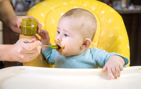 Little baby is eating broccoli vegetable puree. Selective focus. people.