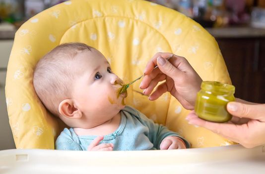 Little baby is eating broccoli vegetable puree. Selective focus. people.