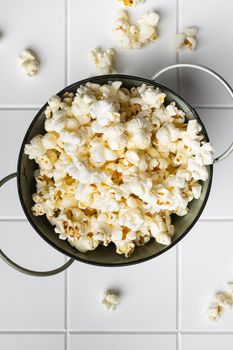 Prepared salted popcorn, on white ceramic squared tile table background, top view flat lay