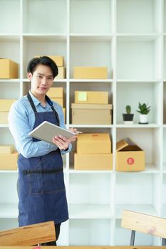 A portrait of a small start-up and SME owner, an Asian male entrepreneur checking orders to organize products before packing them into inner boxes for customers.