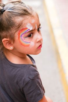 Santa Pola, Alicante, Spain- July 2, 2022: LIttle girl with colorful make up attending Gay Pride Parade with rainbow flags, banners and colorful costumes