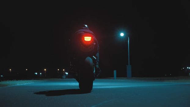 A man moving away on a sports motorcycle into the distance against the backdrop of a night city in 4k