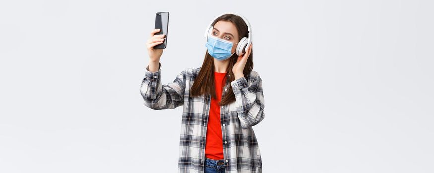 Social distancing, leisure and lifestyle on covid-19 outbreak, coronavirus concept. Woman in headphones and medical mask listening music, taking selfie on mobile phone using filters.