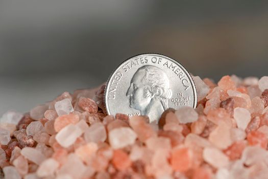 Salt price. Large crystals of pink Himalayan salt, close-up. A coin in a pile of salt as a symbol of rising prices