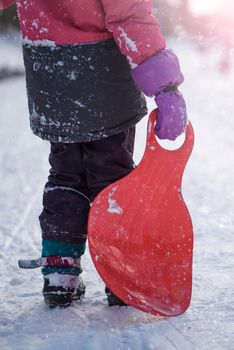 The girl is holding a red sled in her hands to ride the hill. Sledging. Activities for children and teenagers. Winter entertainment and sports