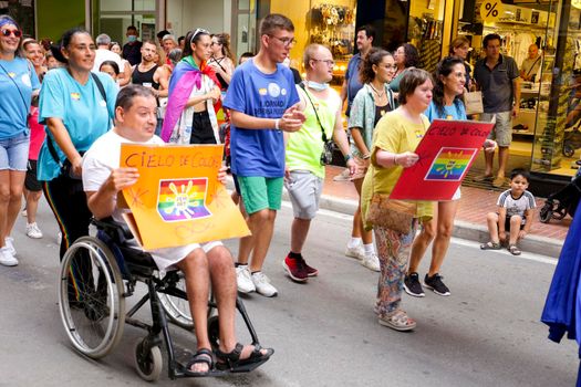 Santa Pola, Alicante, Spain- July 2, 2022: Spanish People with disabilities attending Gay Pride Parade with rainbow flags, banners and colorful costumes