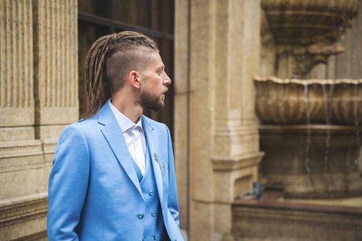 Caucasian man with dreadlocks in blue three piece business suit, outdoor portrait.