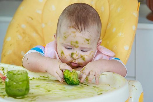 Little baby eats broccoli puree himself. Selective focus. People.