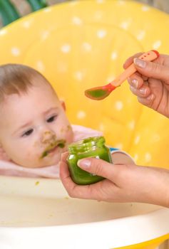 Little baby is eating broccoli vegetable puree. Selective focus. People.