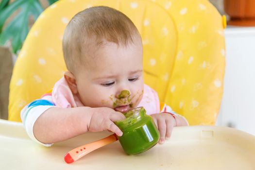 Little baby is eating broccoli vegetable puree. Selective focus. People.