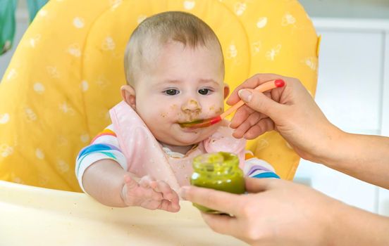 Little baby is eating broccoli vegetable puree. Selective focus. People.