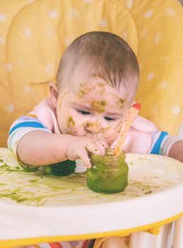 Little baby eats broccoli puree himself. Selective focus. People.