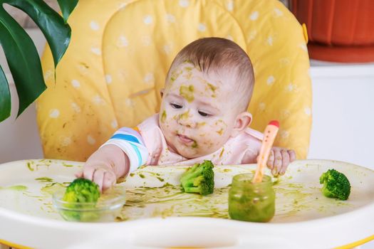 Little baby eats broccoli puree himself. Selective focus. People.