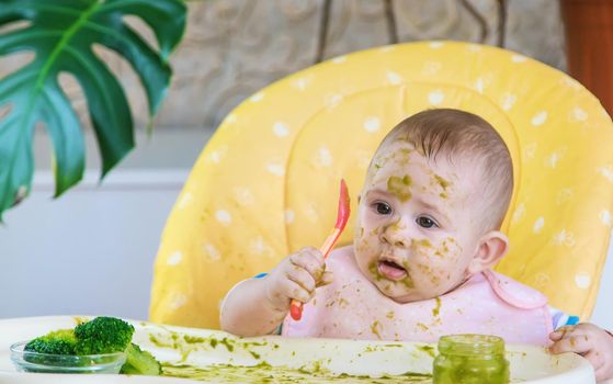 Little baby eats broccoli puree himself. Selective focus. People.