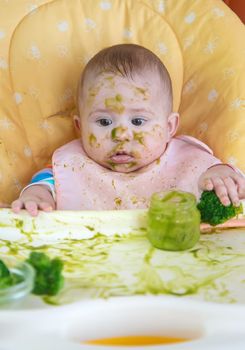 Little baby eats broccoli puree himself. Selective focus. People.