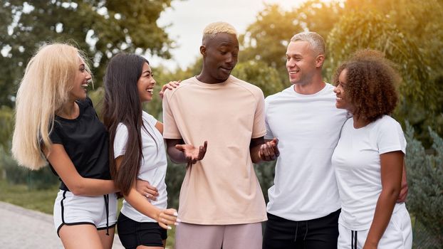 Multi-ethnic group teenage friends. African-american asian caucasian student spending time together Multiracial friendship Happy smiling People dressed black white sportswear meeting outdoor