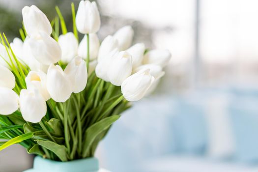White tulip flowers in vase standing coffee table with blurred interior background. Spring flowers