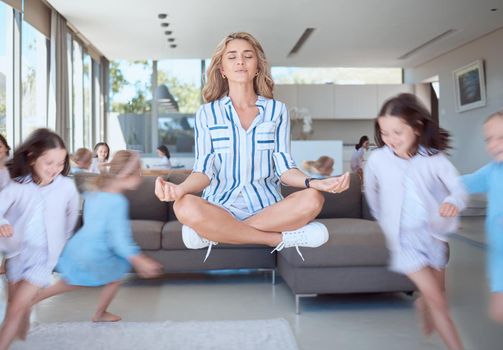 Young mother meditating for stress relief while her energetic kids run around her. Calm mom with naughty mischievous children running around her in the living room at home.
