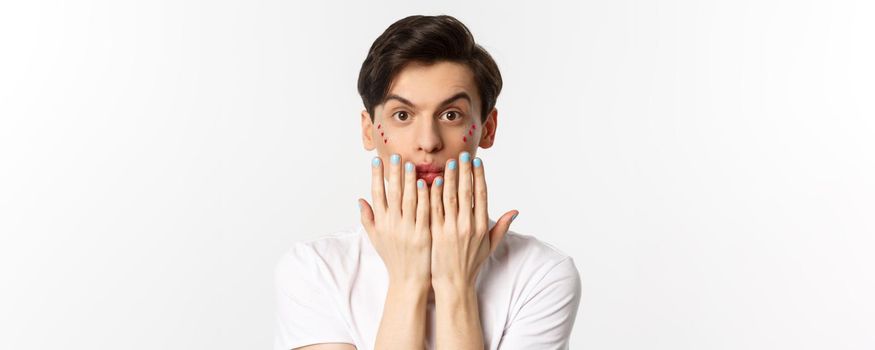 People, lgbtq and beauty concept. Beautiful gay man showing blue nail polish on fingernails and looking at camera, have manicure, standing over white background.