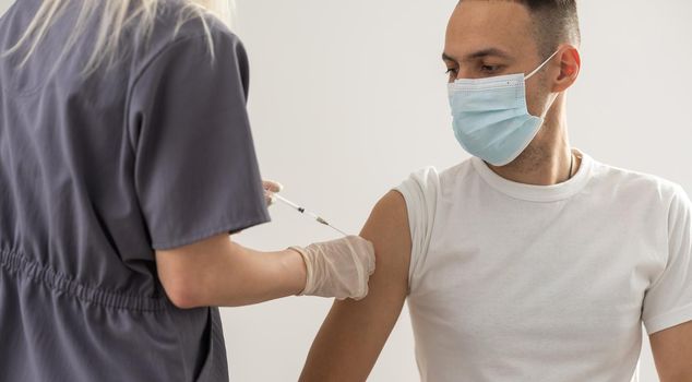 woman doctor in a protective face mask makes vaccination to european man in hospital.