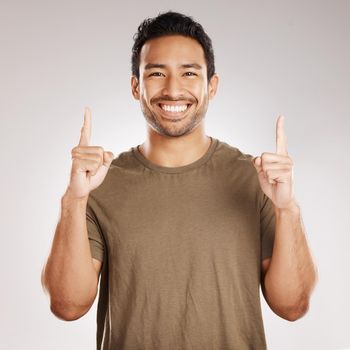 Handsome young mixed race man pointing towards copyspace while standing in studio isolated against a grey background. Happy hispanic male advertising or endorsing your product, company or idea.
