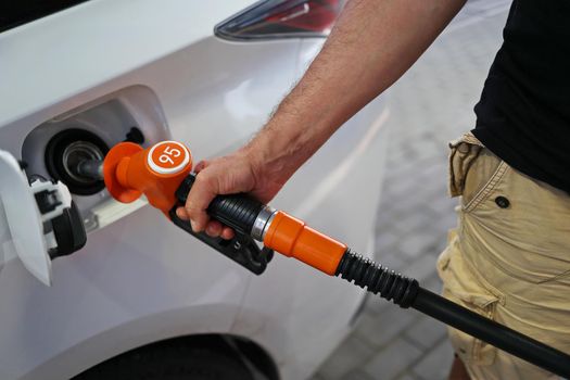 man's hand holds a filling pistol inserted into the gas tank hole of a car at a gas station. Close-up of a hand and a refueling gun. The concept of the high cost of fuel, inside out empty pockets.