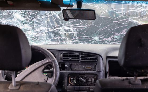 Damaged car window after an accident. Broken windshield as a result of an accident, inside view. Cabin interior details, view from the cab. Safe movement. Broken windshield. Glass crack and damage