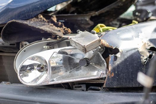 Broken headlights as a result of a collision. Broken blue car after an accident. Car accident concept. Damaged emergency headlight, hood and bumper. Damage to the body of the car after the accident