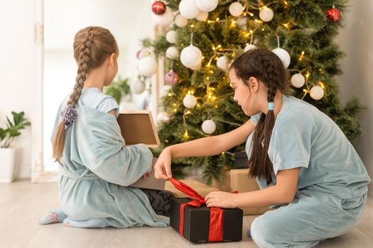 Two little girls open Christmas present under the Christmas tree.