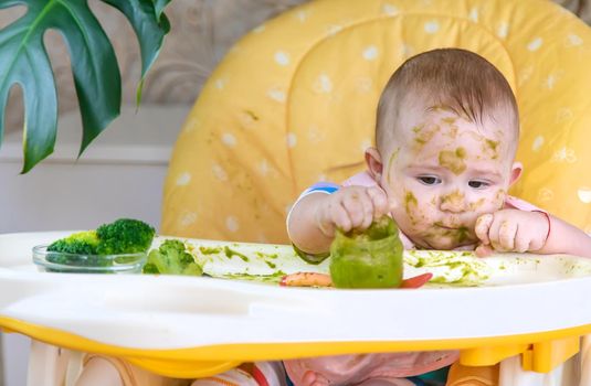 Little baby eats broccoli puree himself. Selective focus. People.