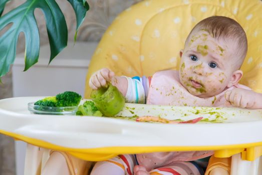 Little baby eats broccoli puree himself. Selective focus. People.