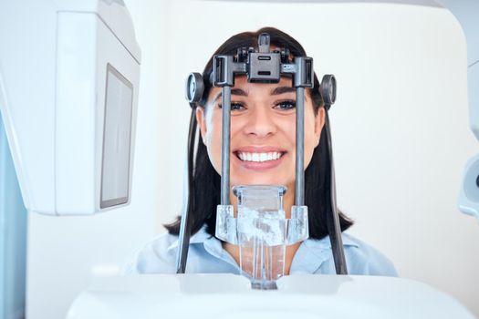 Young woman smiling and standing with her head in a panoramic dental xray machine. Getting her mouth checked at a visit to the dentist. Keep your teeth healthy and strong. Oral hygiene is important.