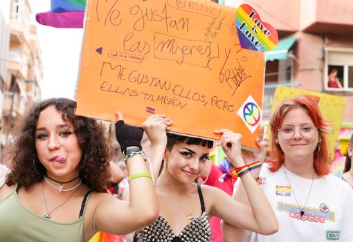 Santa Pola, Alicante, Spain- July 2, 2022: Spanish People attending Gay Pride Parade with rainbow flags, banners and colorful costumes